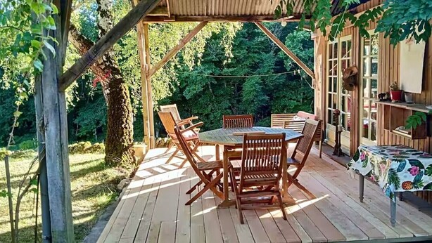 A wooden deck with a table and chairs, surrounded by greenery. - Holiday Home “La Voyageuse” with Private Terrace, Garden & Wi-Fi (Gorses)