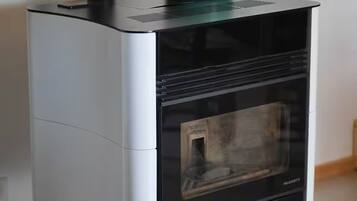 A modern, compact wood stove with a teal kettle on top, a glass door, and a sleek black and white design.