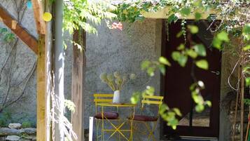 Un espace extérieur aménagé dans un style rustique, avec une table et des chaises en bois, un vase rempli de fleurs et un mur en pierre en arrière-plan.