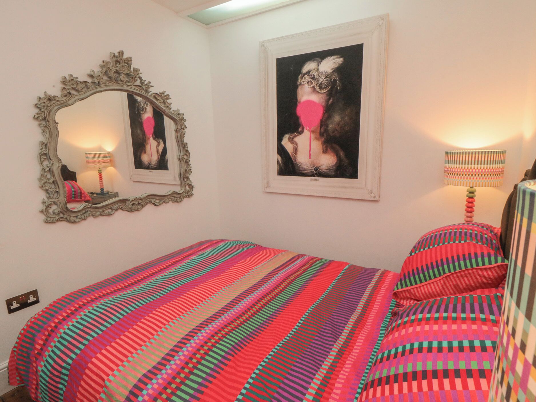 Quarto com cama, espelho, duas fotos emolduradas e abajur.