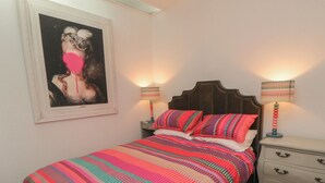 Un dormitorio con una cama, dos mesitas de noche con lámparas, un aparador y un cuadro en la pared.