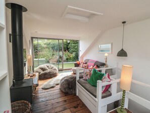 A cozy room with a fireplace, a sofa with cushions, a lamp, and a view of a garden through a sliding door. - Hillsover (Saltburn-by-the-Sea)