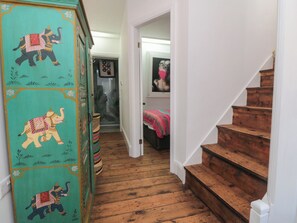 A hallway with a teal-colored cabinet featuring elephant designs, a wooden staircase, and a door leading to a room with a bed. - Hillsover (Saltburn-by-the-Sea)