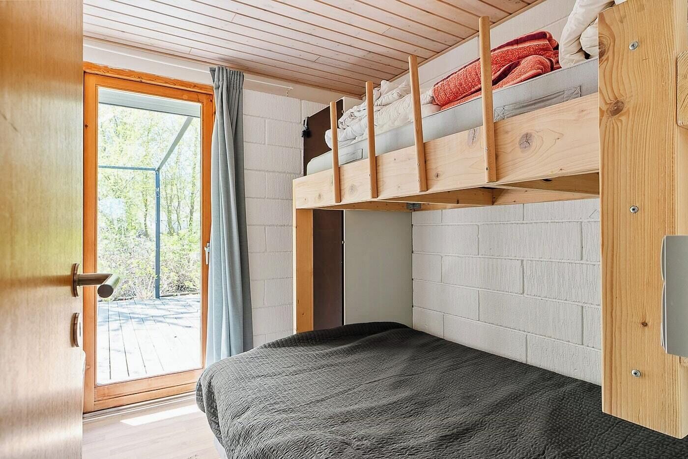A room with a bunk bed, a single bed, a wooden door, and a view through a window.