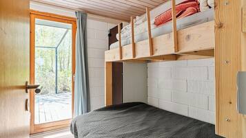 A room with a bunk bed, a single bed, a wooden door, and a view through a window.