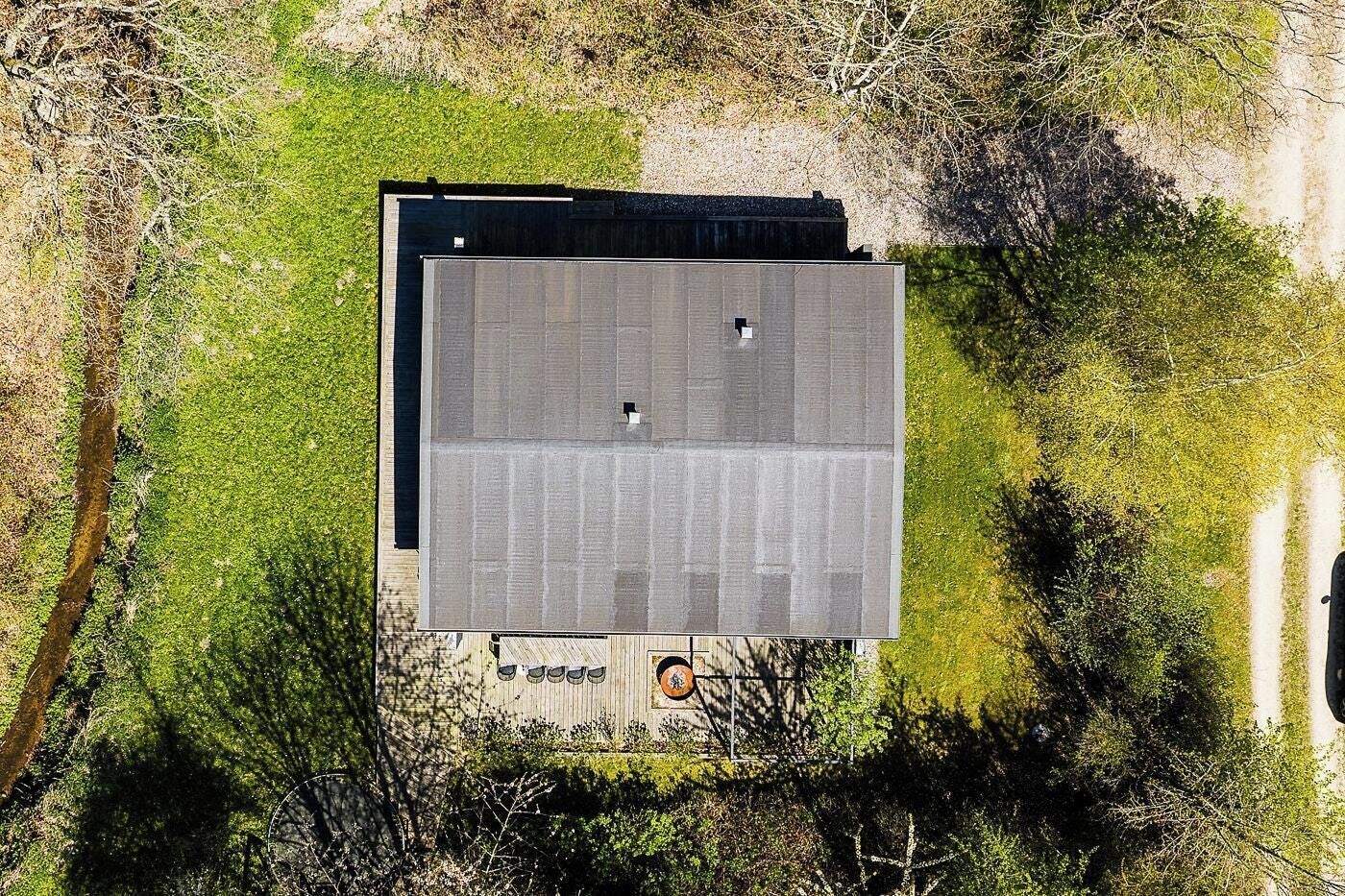 An aerial view of a building with a flat roof, surrounded by greenery and a dirt path.