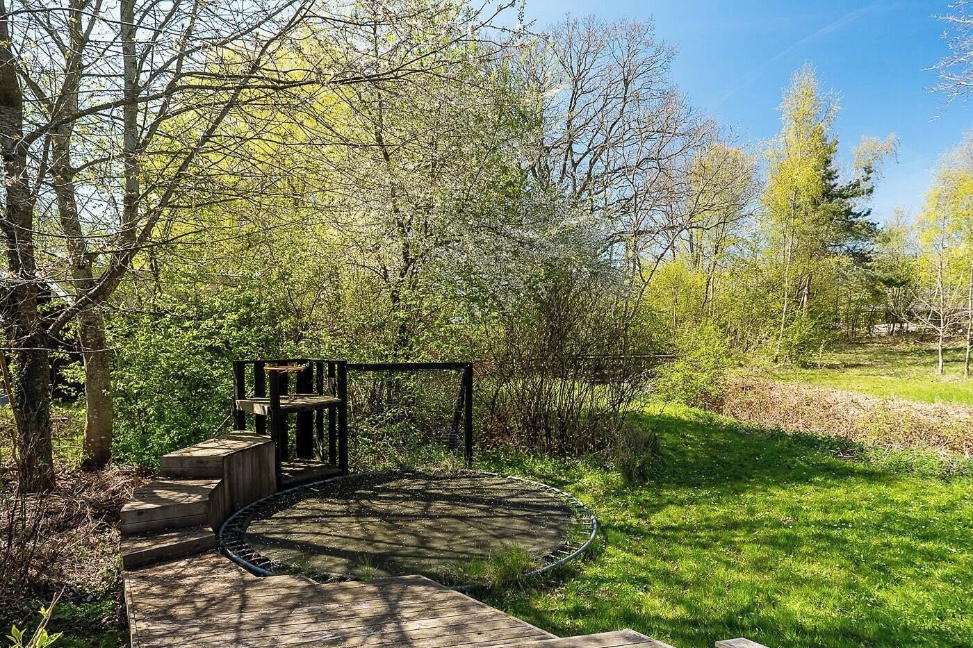 Eine Holzterrasse mit einem runden Steinbecken, umgeben von Bäumen und Gras.
