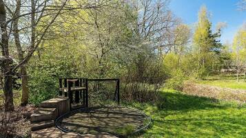 Eine Holzterrasse mit einem runden Steinbecken, umgeben von Bäumen und Gras.