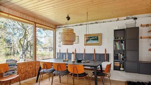 Un coin repas avec une table en bois, des chaises orange, un luminaire suspendu et une bibliothèque.