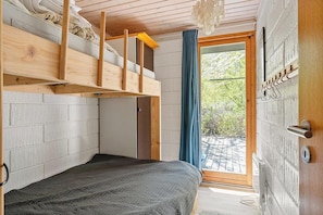 A bedroom with a bunk bed, a sliding door, a view of greenery, and a wooden ceiling.
