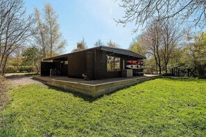 Eine moderne Holzhütte mit überdachter Veranda, Garage und kleiner Sitzgelegenheit im Freien.