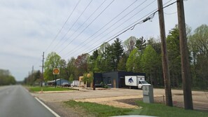 A roadside view with a gravel parking area, a Shell gas station sign, a building with a sign 'Plumbing,' and a utility box. - Brand new construction quiet neighborhood fire pit screened porch (Sawyer)