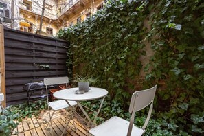 Eine kleine Terrasse im Freien mit einem runden Tisch und zwei Stühlen, umgeben von einem Holzzaun und einer mit Efeu bewachsenen Mauer.