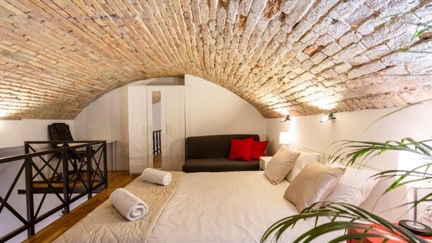 Une chambre avec un plafond en briques, un lit, un canapé, un bureau et une plante.