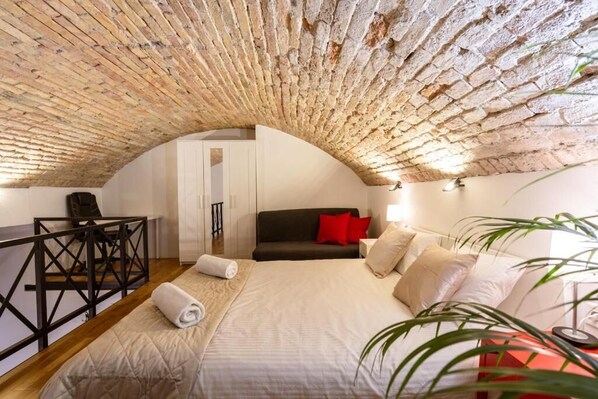 Ein Schlafzimmer mit Ziegeldecke, einem Bett, einem Sofa, einem Schreibtisch und einer Pflanze.