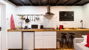 Une cuisine compacte équipée d’un four à micro-ondes, d’une cuisinière et de casseroles suspendues. On y trouve également des tabourets et un petit réfrigérateur.