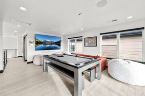 Un salon moderne doté d’une table de billard, d’un grand téléviseur à écran plat et d’un coin salon confortable.