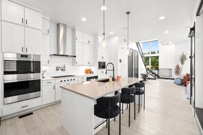 Une cuisine moderne avec des meubles blancs, des appareils en acier inoxydable et un îlot central doté de tabourets de bar.