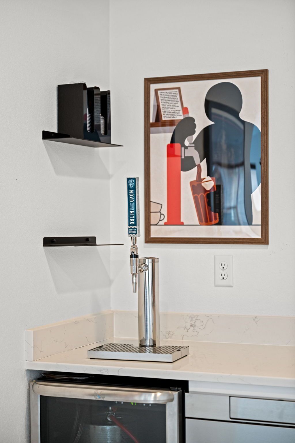 A kitchen with a coffee machine, a framed artwork, and a small shelf with books.