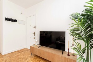 A modern living room with a wooden entertainment unit, a flat-screen TV, a door with a handle, and a potted plant. - Descubre este elegante apartamento de una habitación doble en Calle Hermosilla, un espacio diseñado para quienes buscan comodidad, estilo y funcionalidad durante largas estancias en Madrid. (MADRID)