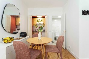 A dining area with a round table, four chairs, a vase, and a bowl of fruit on a white counter. - Descubre este elegante apartamento de una habitación doble en Calle Hermosilla, un espacio diseñado para quienes buscan comodidad, estilo y funcionalidad durante largas estancias en Madrid. (MADRID)