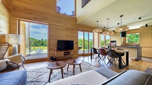 A spacious living area with a large TV, wooden flooring, and a dining area with chairs and a table. - Villa Lovelos with Infinity Pool in Nature (Lovinac)