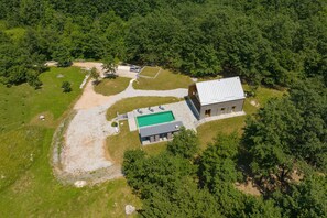 An aerial view of a property with a swimming pool, a large building, and surrounding forested area.