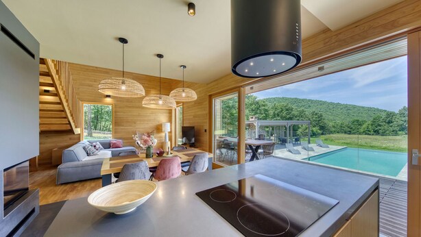 A modern kitchen with a large island, dining area, and a view of a swimming pool. - Villa Lovelos with Infinity Pool in Nature (Lovinac)