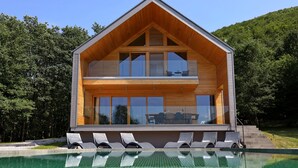 A modern two-story house with a large balcony, a swimming pool, and lounge chairs. - Villa Lovelos with Infinity Pool in Nature (Lovinac)