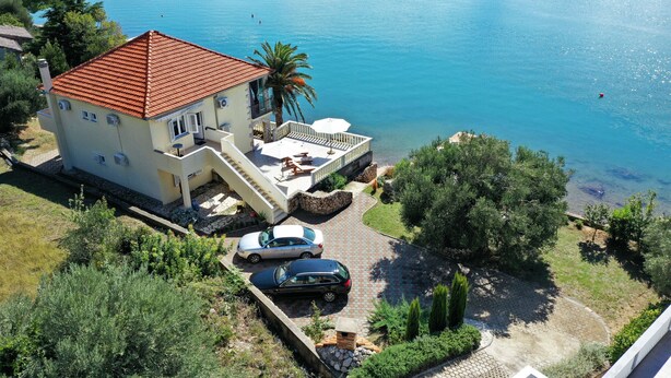 A two-story house with a red-tiled roof, a balcony, and a paved driveway with two cars parked. - Apartment Laura 1 by the Sea (Maslenica)