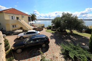 Ein Haus mit rotem Ziegeldach, einer gepflasterten Auffahrt, zwei geparkten Autos und Blick auf ein Gewässer.