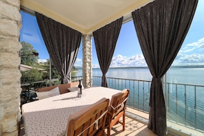 Ein Balkon mit Tisch und Stühlen, einer Flasche und Blick auf das Meer.