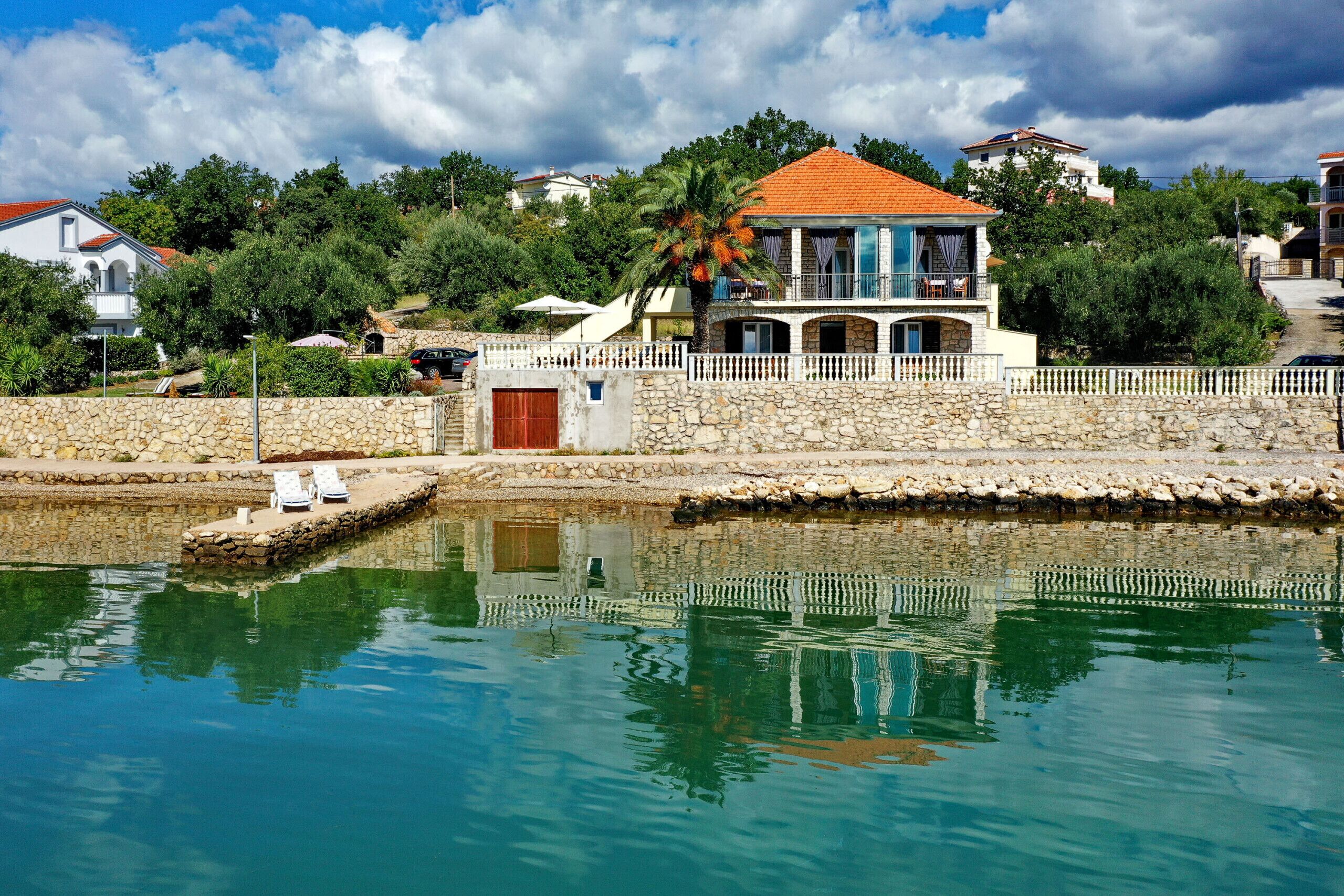 Una villa costera con muro de piedra, piscina y vista al mar.