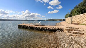 Una spiaggia con sassolini, sedie a sdraio e un muro in pietra.