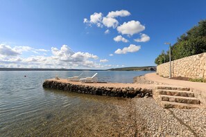 Ein Kiesstrand mit Liegestühlen und einer Steinmauer.