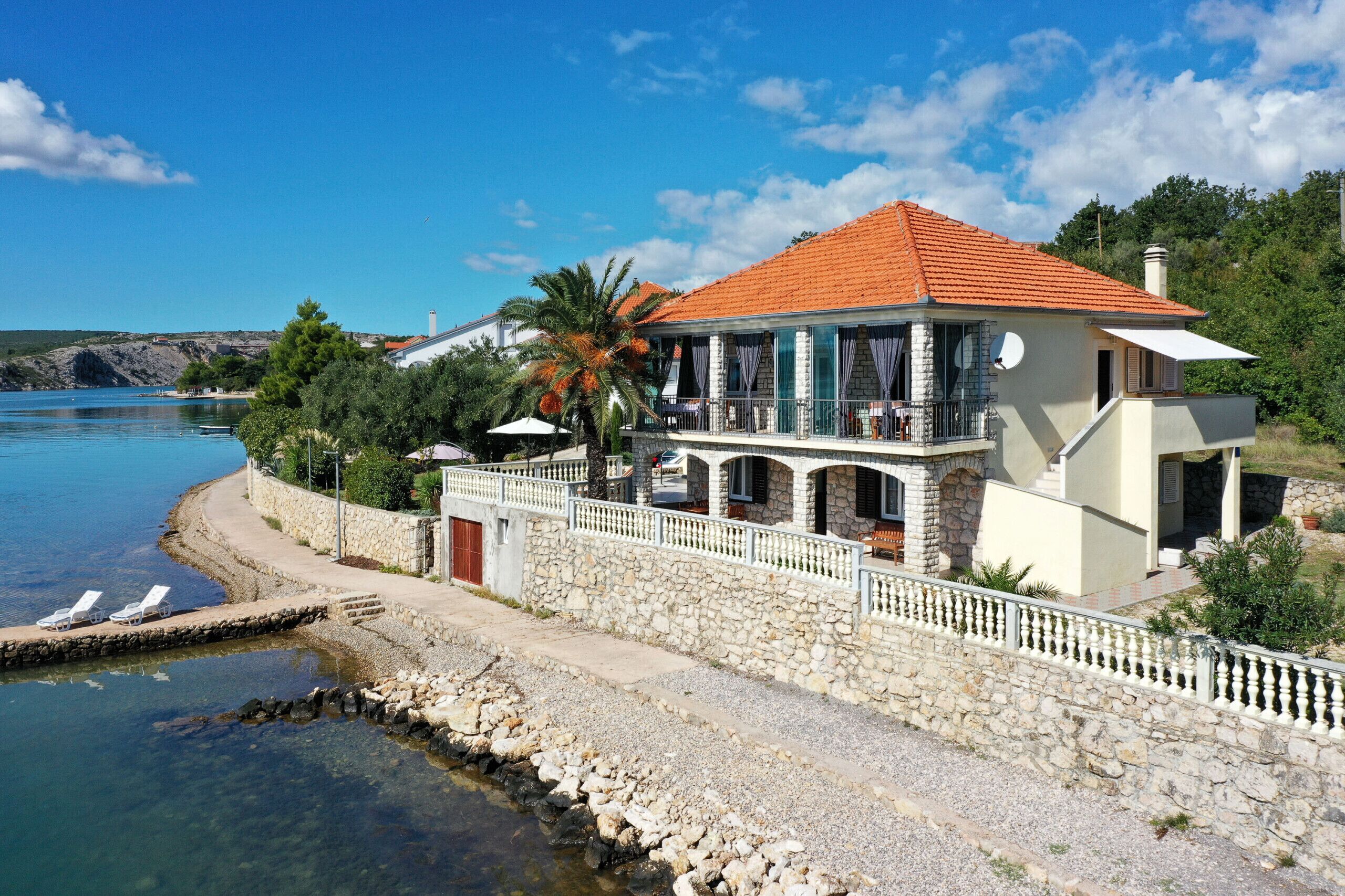 A coastal house with a stone wall, a balcony, and a view of the sea.