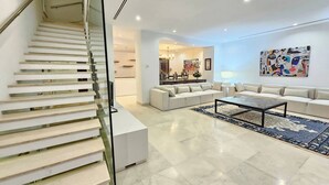 A modern living room with a glass staircase, a sectional sofa, a coffee table, and a large abstract painting on the wall. - Luxurious 7-bedroom Villa in La Marsa, Tunisia - Modern Comfort & Elegance (La Marsa)