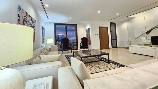 A modern living room with a sofa, a coffee table, and a lamp. There is a large window with blinds, a door, and a staircase. - Luxurious 7-bedroom Villa in La Marsa, Tunisia - Modern Comfort & Elegance (La Marsa)