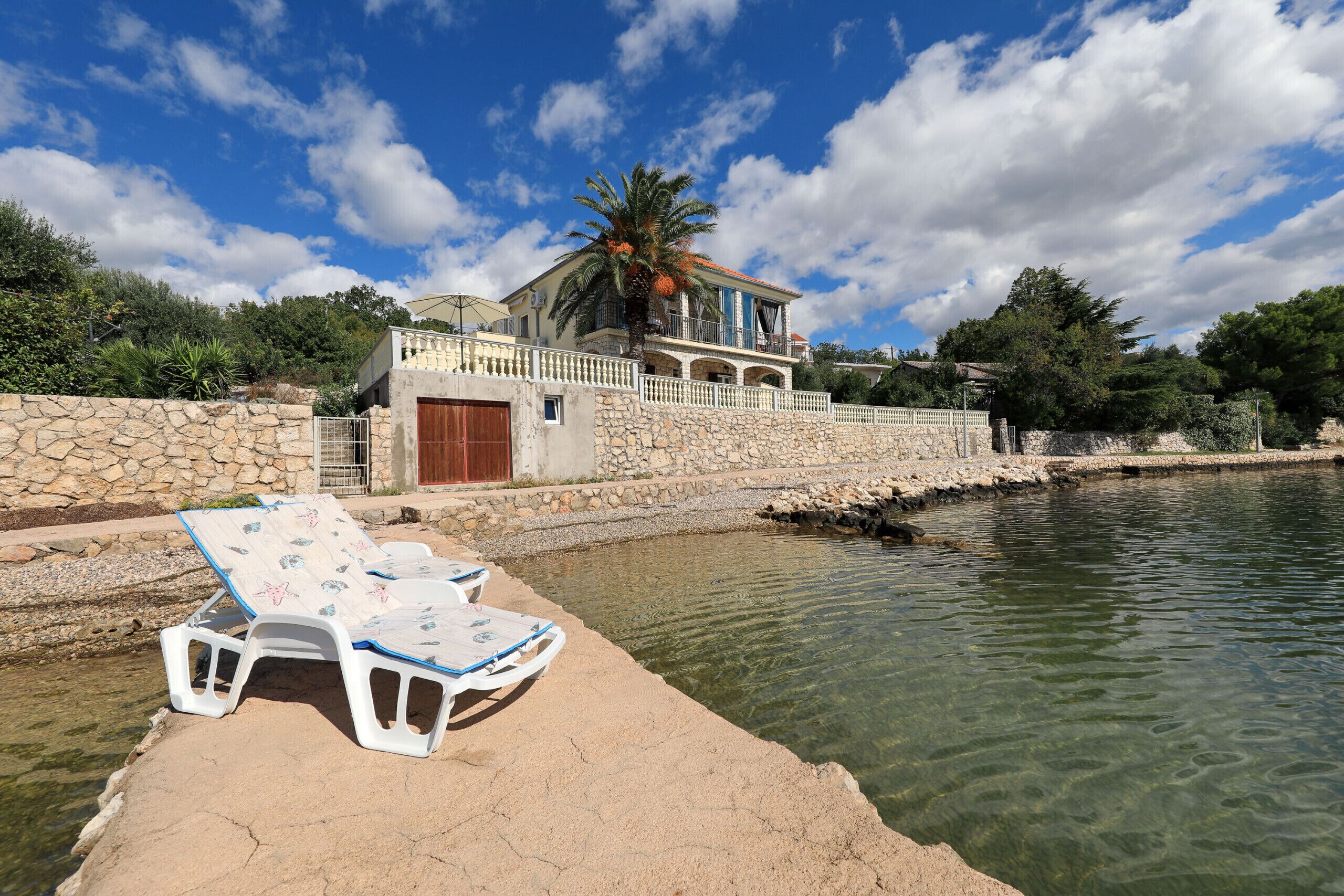 A house with a stone wall, a pool, and lounge chairs.