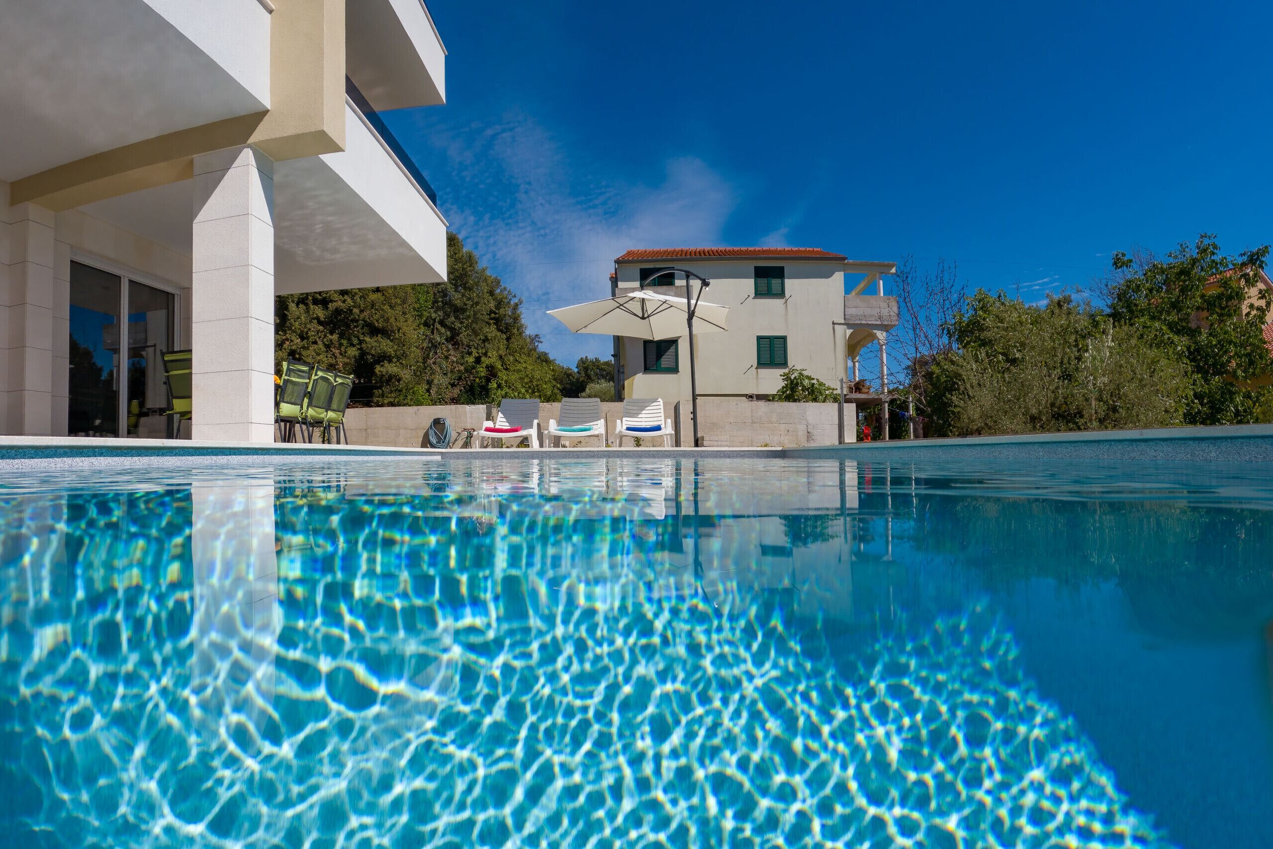 A swimming pool with clear water, a modern building with a red roof, and outdoor seating.