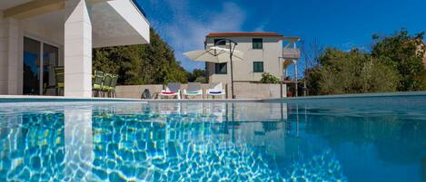 A swimming pool with clear water, a modern building with a red roof, and outdoor seating.