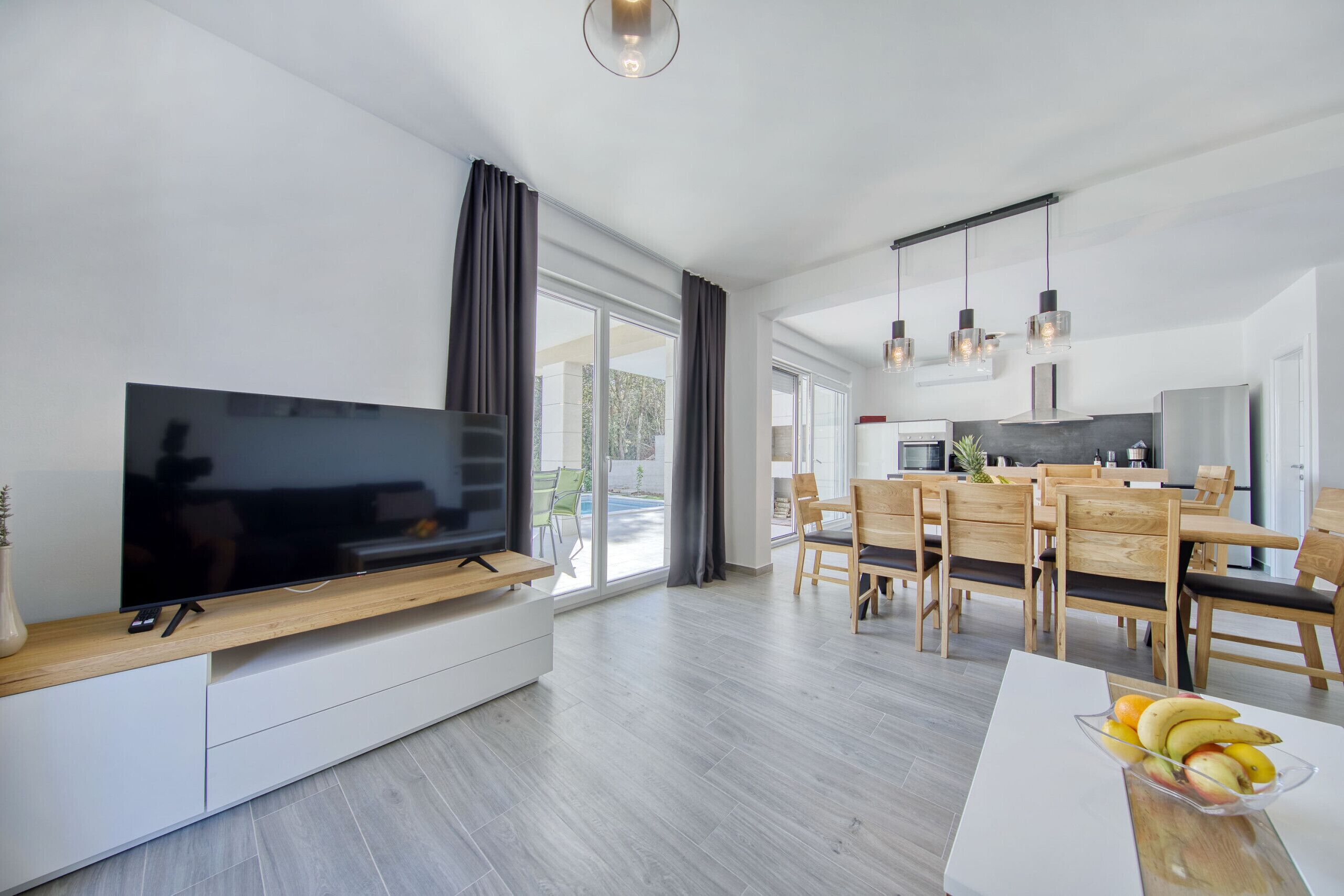 Ein modernes Wohnzimmer mit Flachbildfernseher, Esstisch aus Holz und Stühlen.