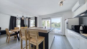 Eine moderne Küche mit Kochinsel, Essbereich mit Stühlen und großen Fenstern mit Blick.