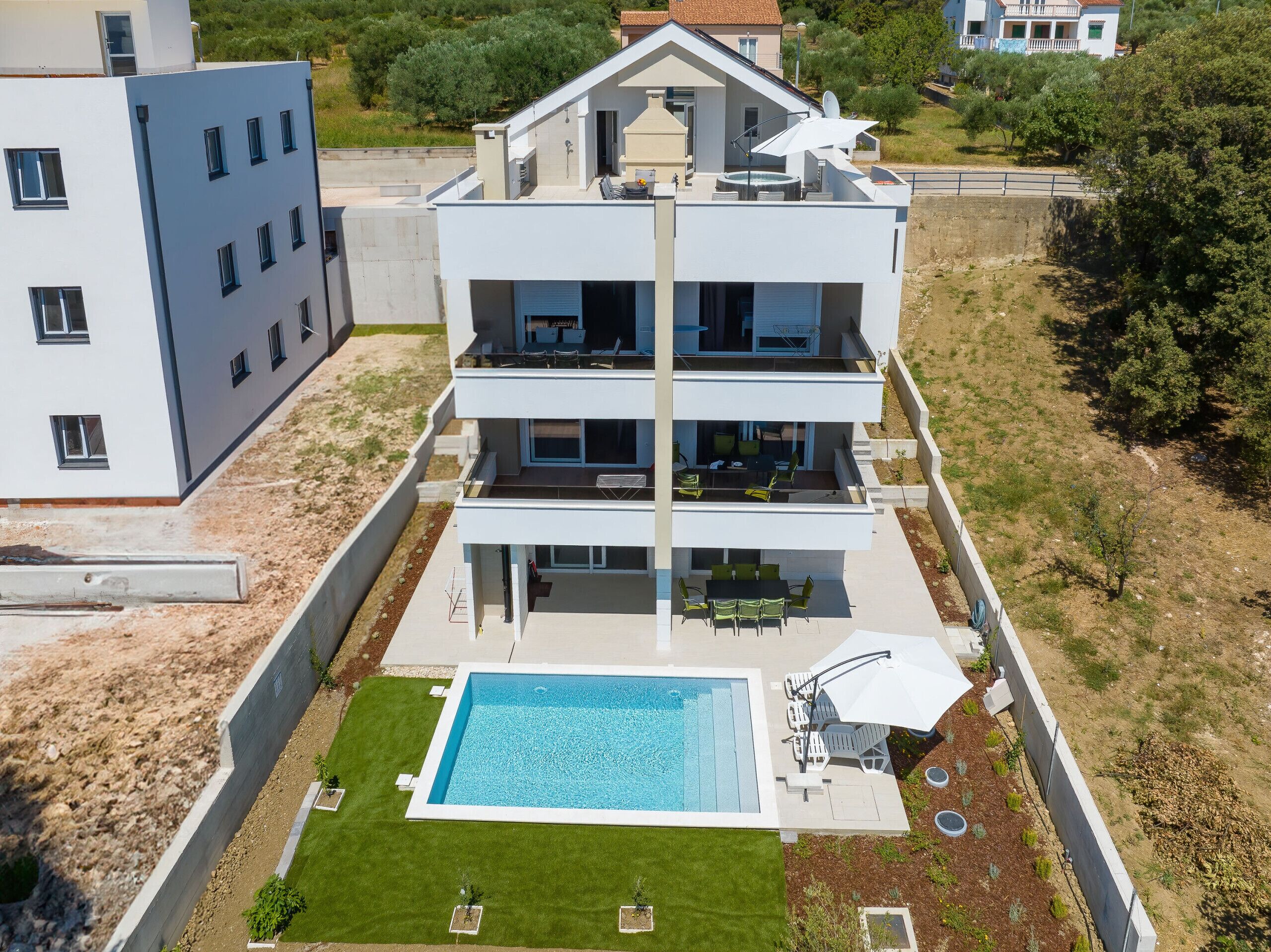 Un edificio residencial de varios pisos con terraza en la azotea, piscina y césped bien cuidado.