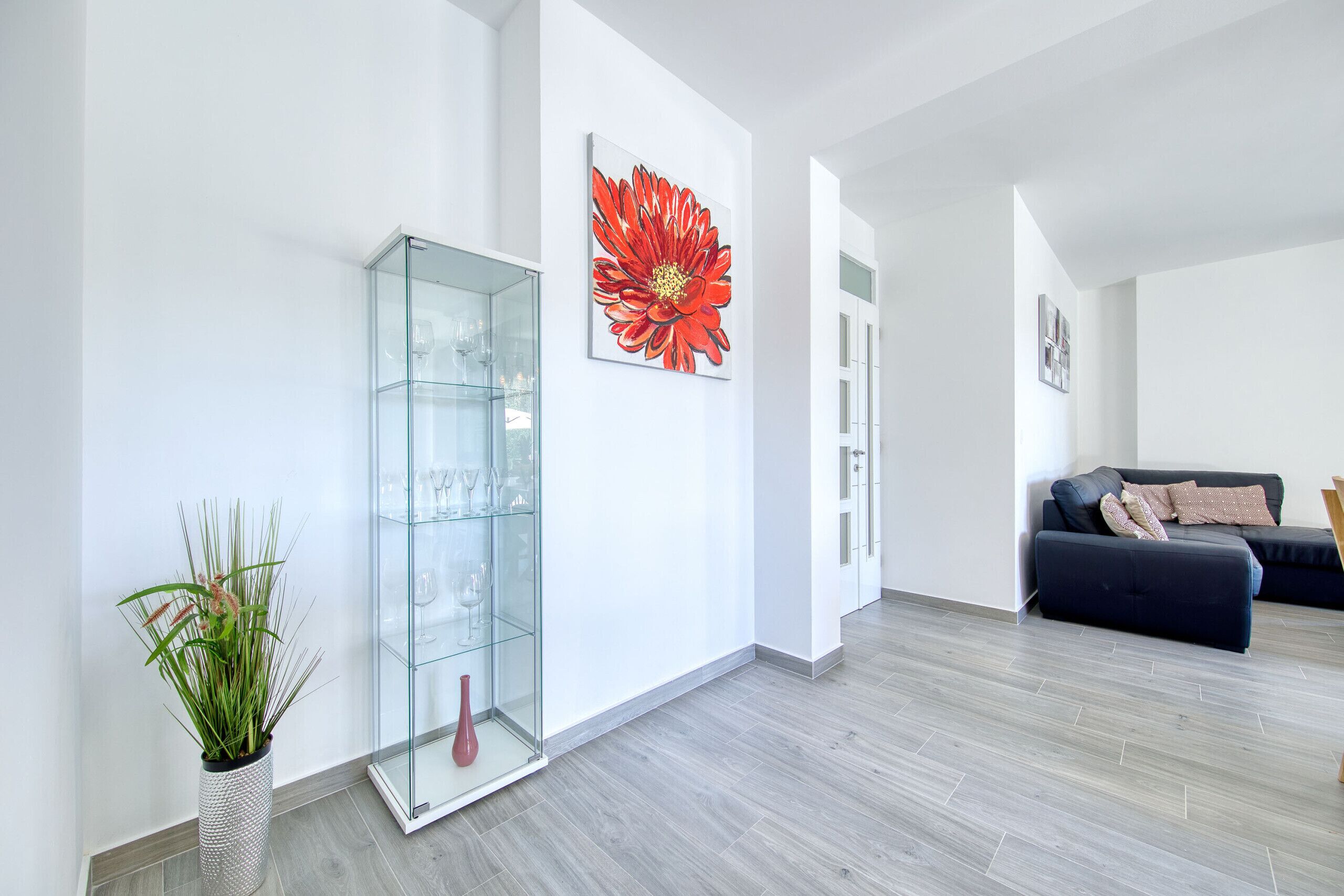A modern living room with a glass cabinet, a large red flower painting, and a dark sofa.