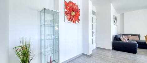 A modern living room with a glass cabinet, a large red flower painting, and a dark sofa.