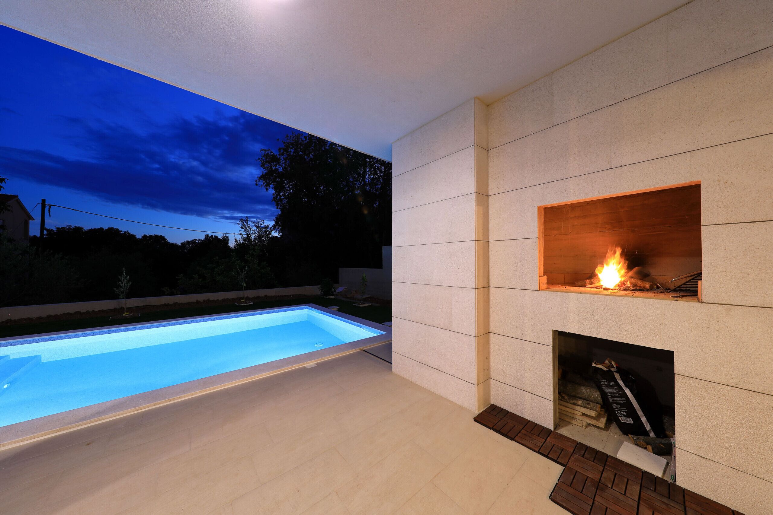 Un área de piscina moderna al aire libre con una chimenea decorativa.