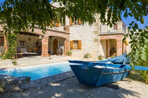 A stone building with a pool, a boat, and outdoor seating. - Villa Gland with Pool and Whirlpool (Nin)