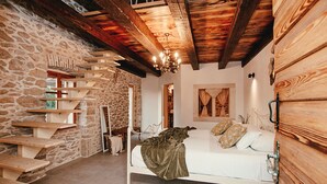 Ein Schlafzimmer mit Steinwand, Holzbalken, einem Bett und einer Treppe.