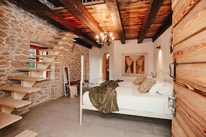 A bedroom with a stone wall, wooden beams, a bed, and a staircase. - Villa Gland with Pool and Whirlpool (Nin)